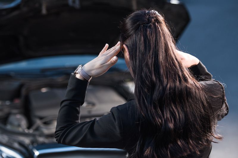 young-troubled-woman-rubbing-temples-while-looking-at-car-engine.jpg